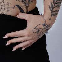 Hopeinen rannekoru Nazar-riipuksella ranteessa, tatuoitu käsi