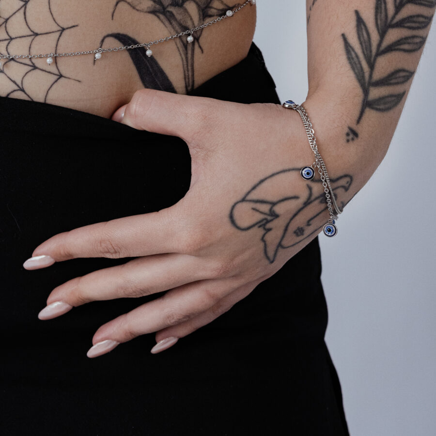 Hopeinen rannekoru Nazar-riipuksella ranteessa, tatuoitu käsi