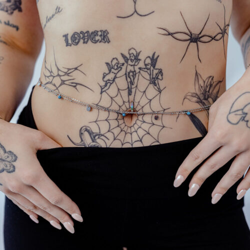 Nainen käyttää kaksirivisiä hopeisia ja kultaisia vatsaketjuja tatuoidun vatsan päällä