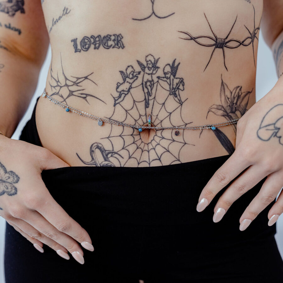 Nainen käyttää kaksirivisiä hopeisia ja kultaisia vatsaketjuja tatuoidun vatsan päällä