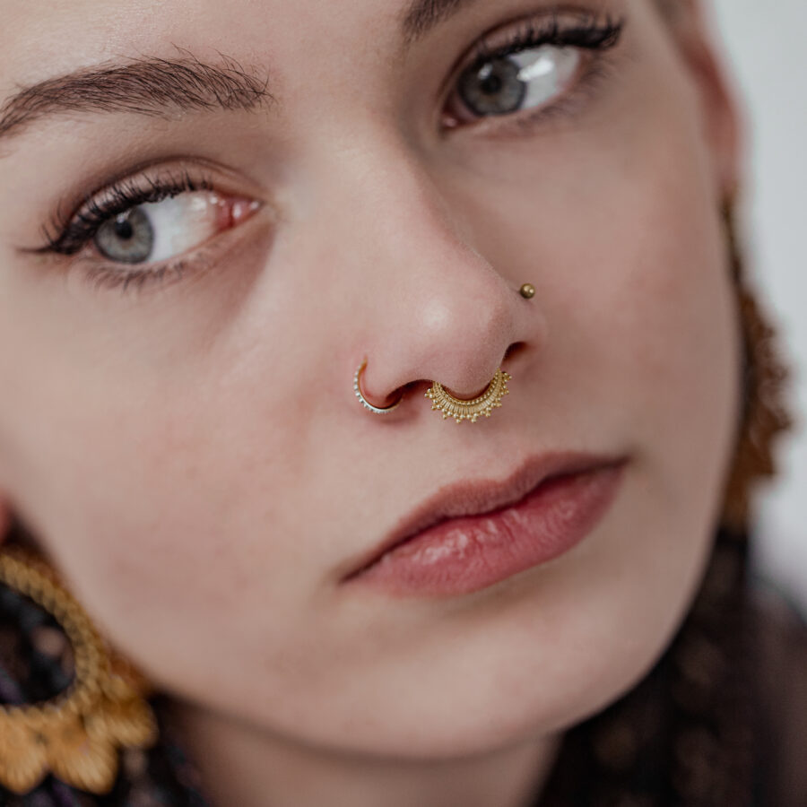 Lähikuva kasvoista, joissa on kultainen septum clicker ja korvakoru