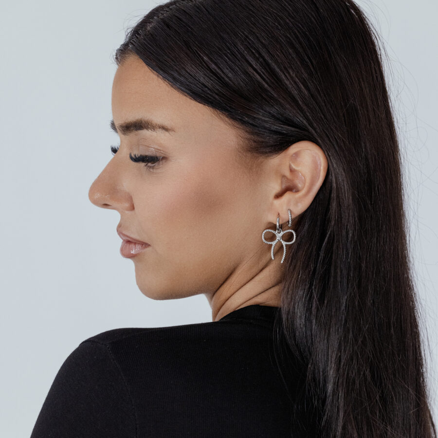 Nainen hopeisilla Little Twisted Bow Hoops -korvakoruilla vaalealla taustalla