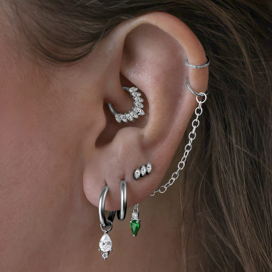 Useita korvakoruja korvassa, mukaan lukien mustat Little Tear Hoops vihreällä kristallilla.
