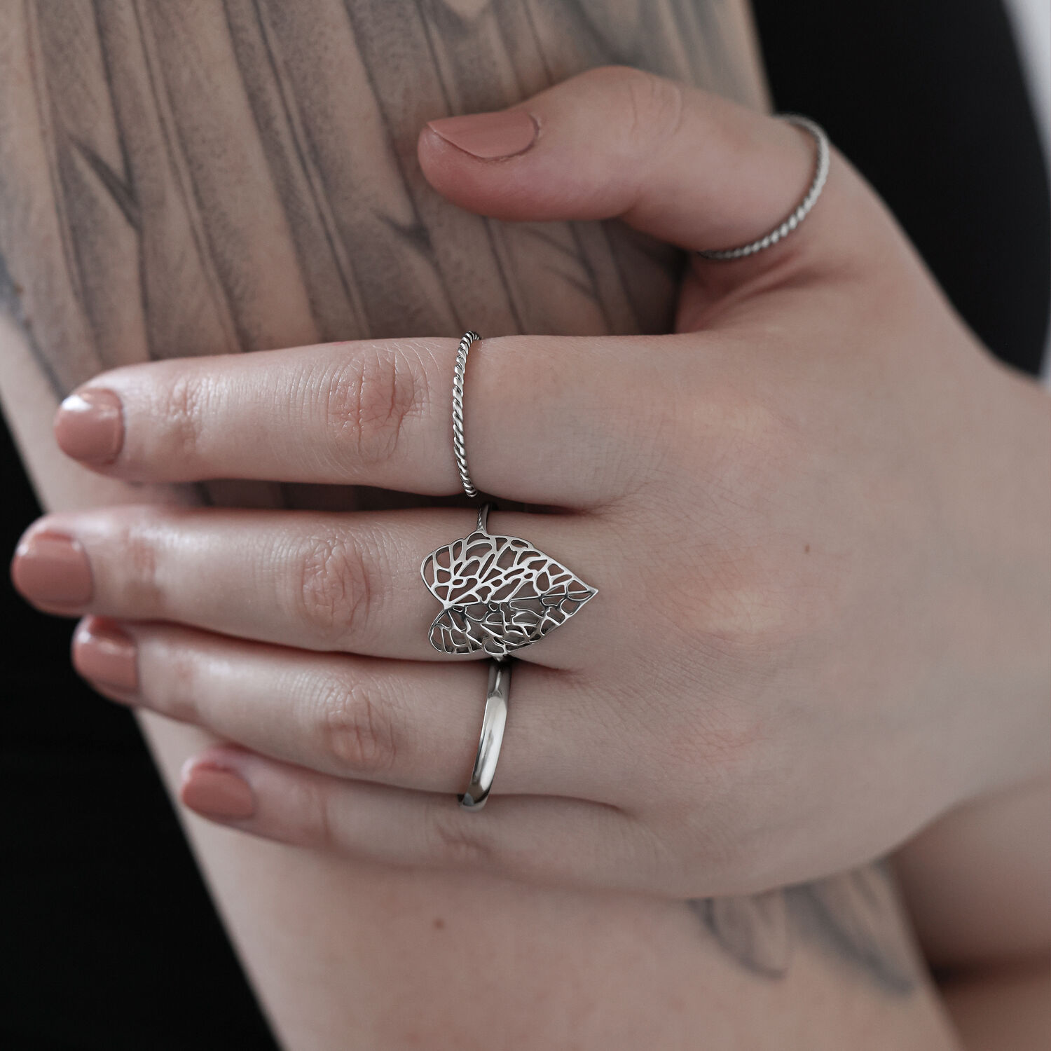 Hopeinen lehtisormus kirurginteräksestä tatuoidulla kädellä vaaleaa taustaa vasten