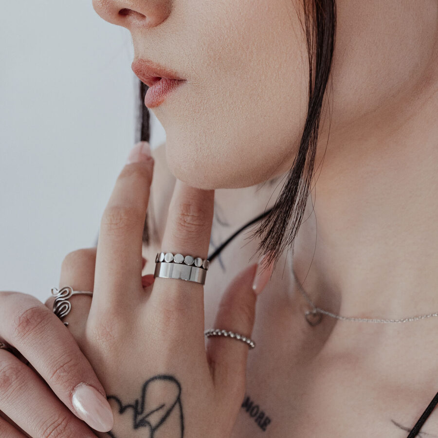 Lähikuva unisex hienosta levykehästä sormessa, hopea, taustalla tatuoitu iho