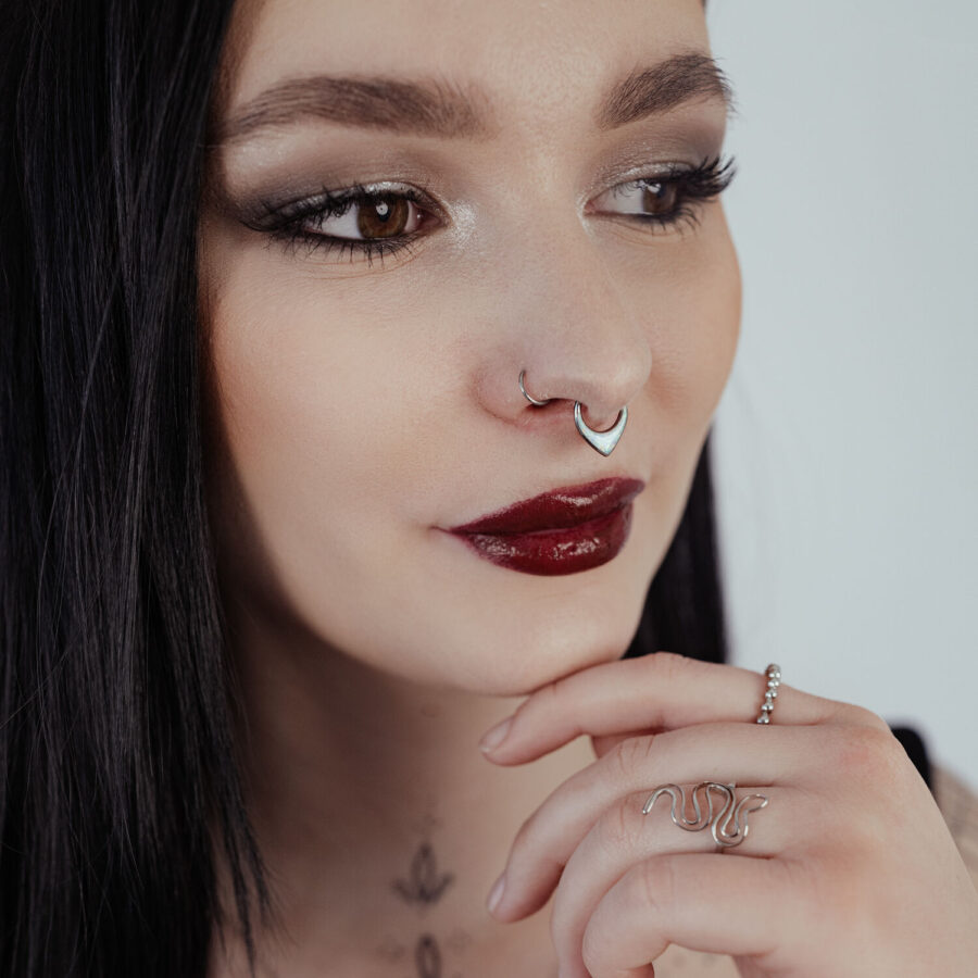 Nainen mustilla hiuksilla käyttää hopeista septum clickeriä opaalilla vaalealla taustalla