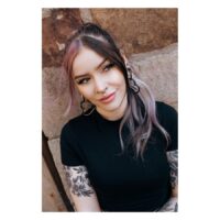 Concaver Septum Clicker mustana käytettynä Nainen mustan Concave Septum Clickerin kanssa ja pitkät hiukset kiviseinän edessä