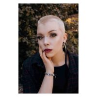 Hopeinen titaani-piercing-kartio ulkona Henkilö, jolla on hopeinen titaani-piercing-kartio ja lyhyt tukka lehtien edessä