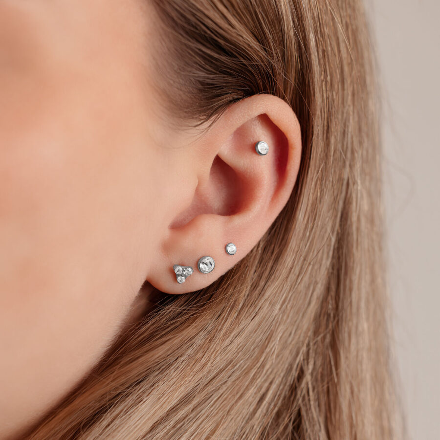 Lähikuva korvasta, jossa hopeinen levy Triple-lävistykseen 4,0 mm koossa vaalealla taustalla