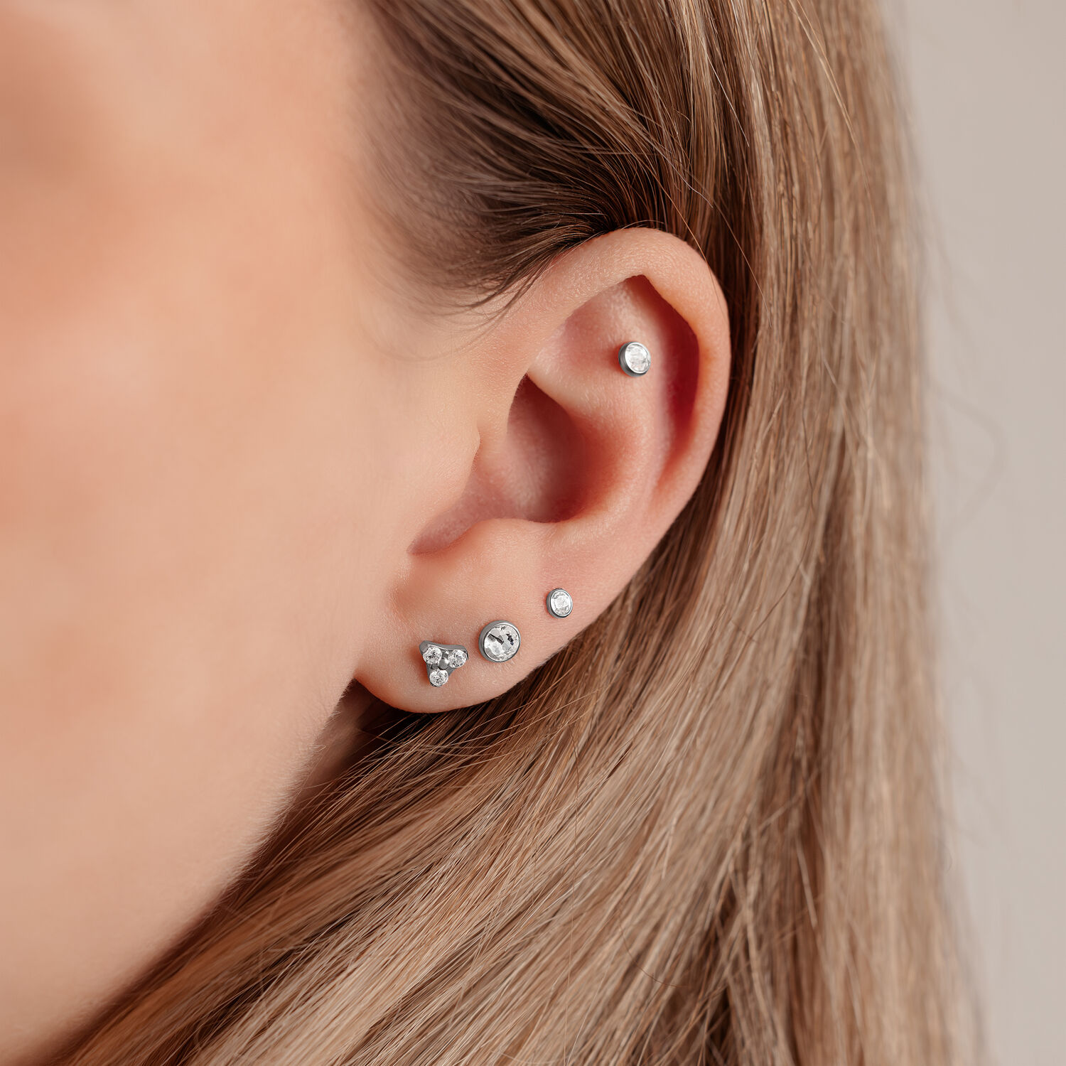 Lähikuva korvasta, jossa hopeinen levy Triple-lävistykseen 4,0 mm koossa vaalealla taustalla