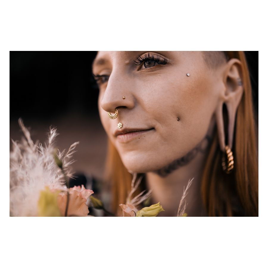 Nainen, jolla on Flower Push-Fit Labret korvassa, kukkien ympäröimänä ulkona