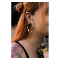 Kultainen Monstera Push-Fit Labret korvassa Punahiuksinen nainen käyttää kultaista Monstera Push-Fit Labret korvassa, tatuoinnit näkyvissä