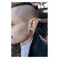 Mies, jolla on hopeiset Ear Saddles korvassa epätarkassa taustassa