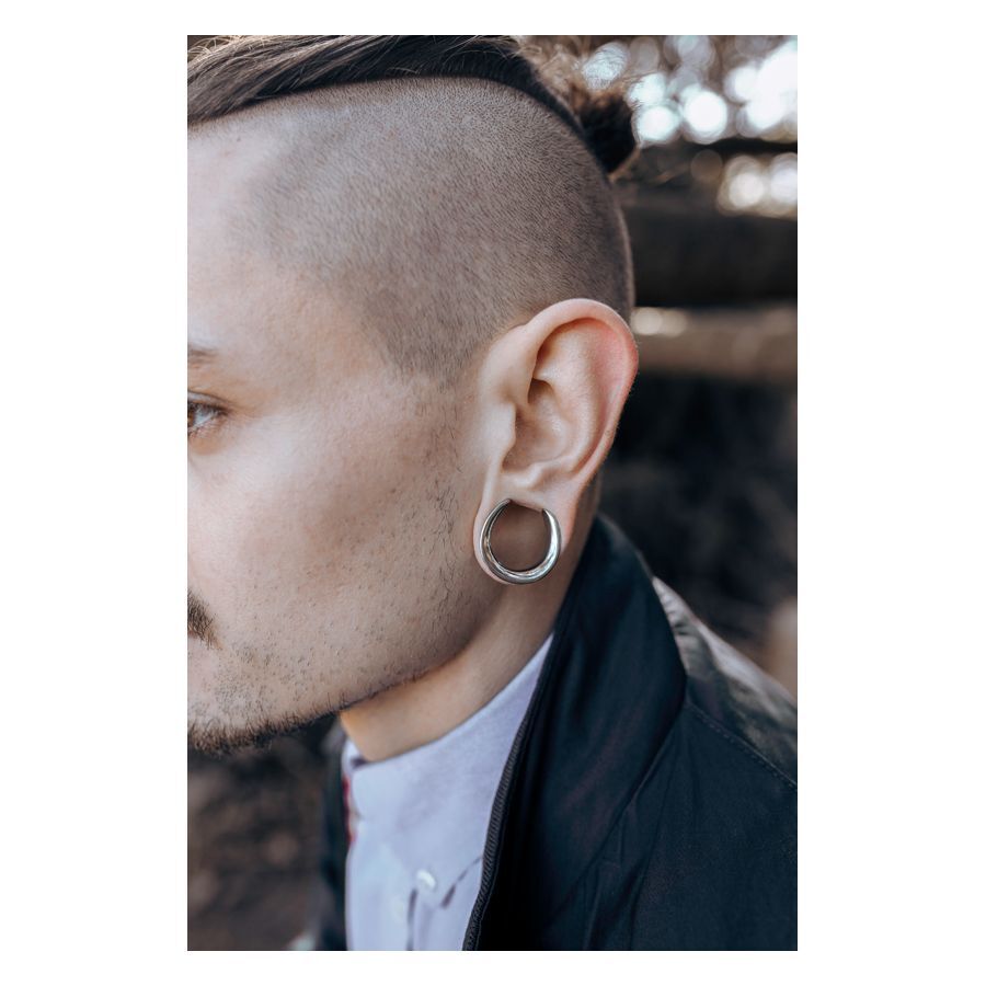 Mies, jolla on hopeiset Ear Saddles korvassa epätarkassa taustassa