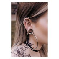 Hopeiset ja mustat Ear Saddles korvassa, jossa on lävistyksiä, taustalla tatuointi