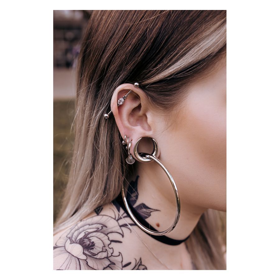 Hopeiset ja mustat Ear Saddles korvassa, jossa on lävistyksiä, taustalla tatuointi