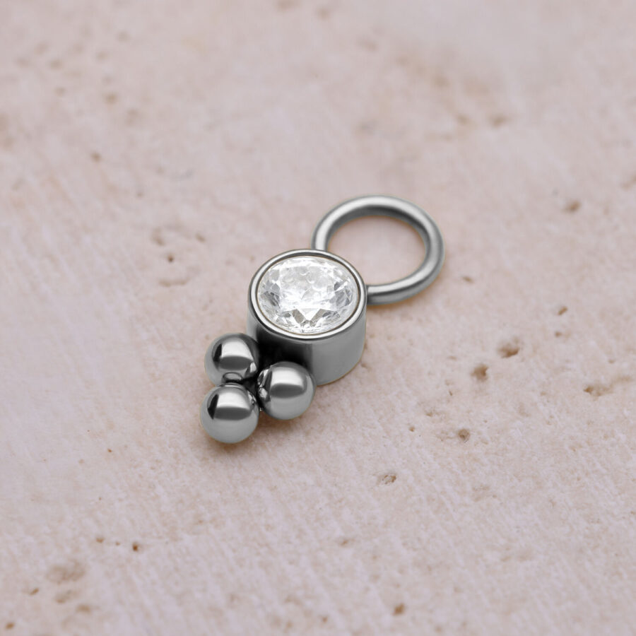 Hopeinen piercing-riipus kristallilla ja palloilla vaalealla taustalla