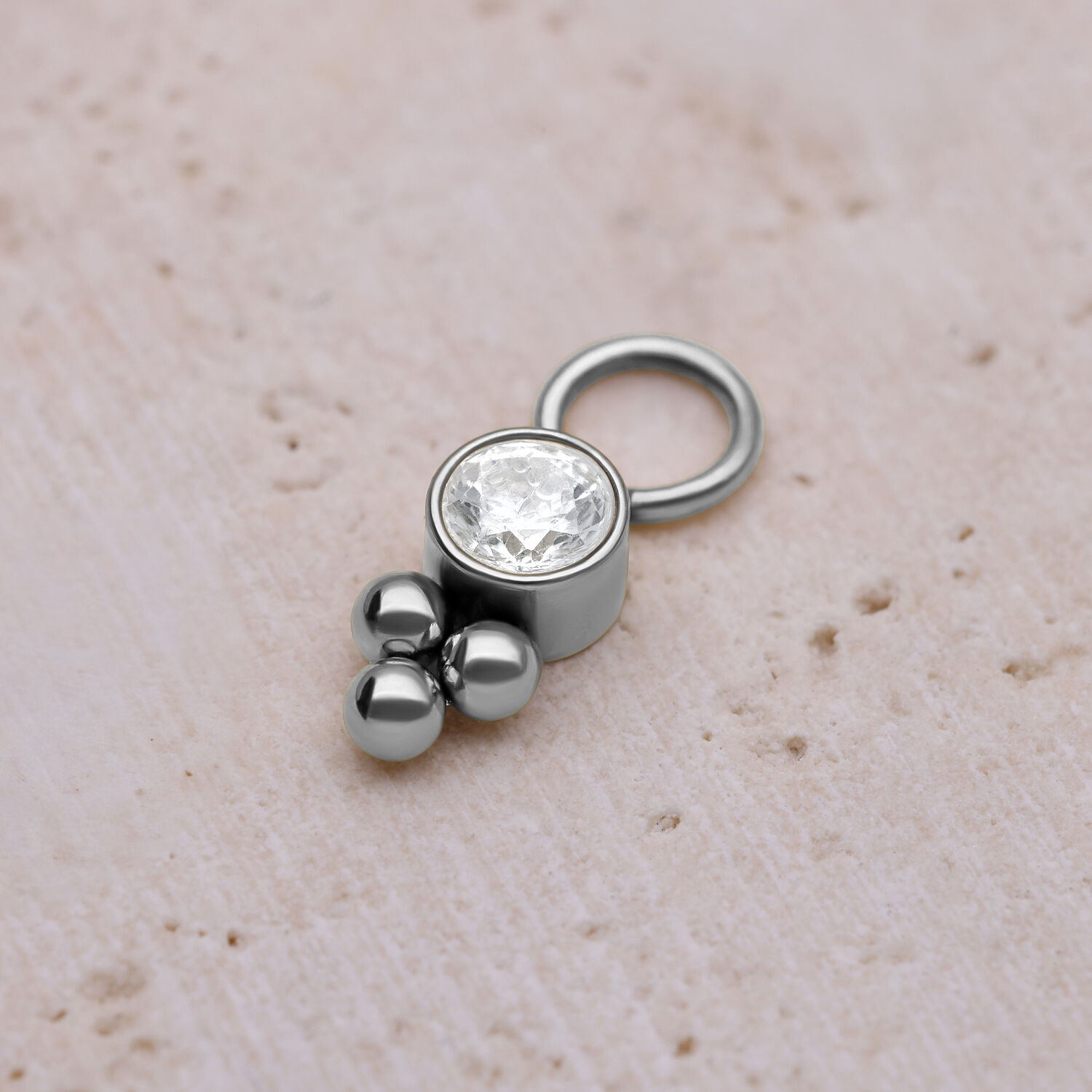 Kristalli-piercing-riipus kirurginteräksestä Hopeinen piercing-riipus kristallilla ja palloilla vaalealla taustalla