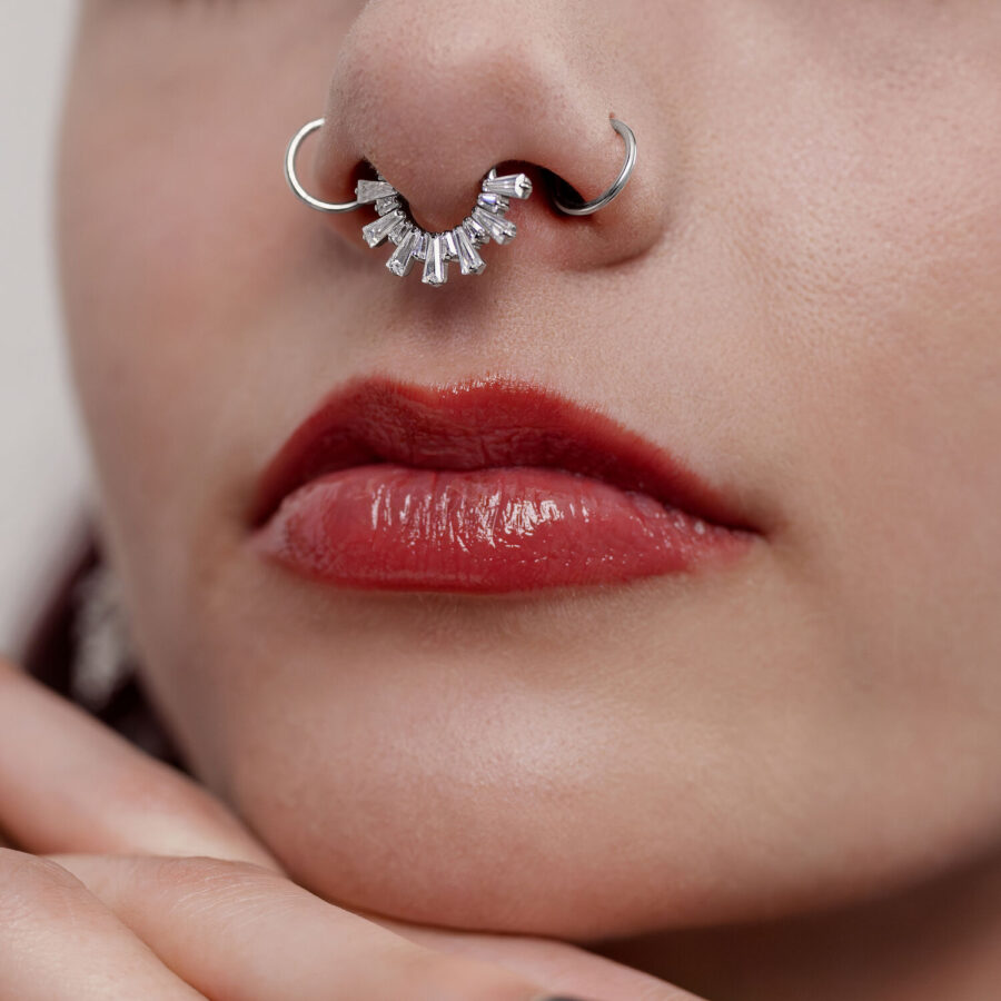 Lähikuva hopeisesta septum clickerista kristalleilla nenässä, näkyvissä punaiset huulet