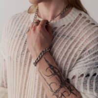 Henkilö, jolla on tatuoitu käsivarsi, käyttää hopeista Chunky-rannekorua ja neulepuseroa