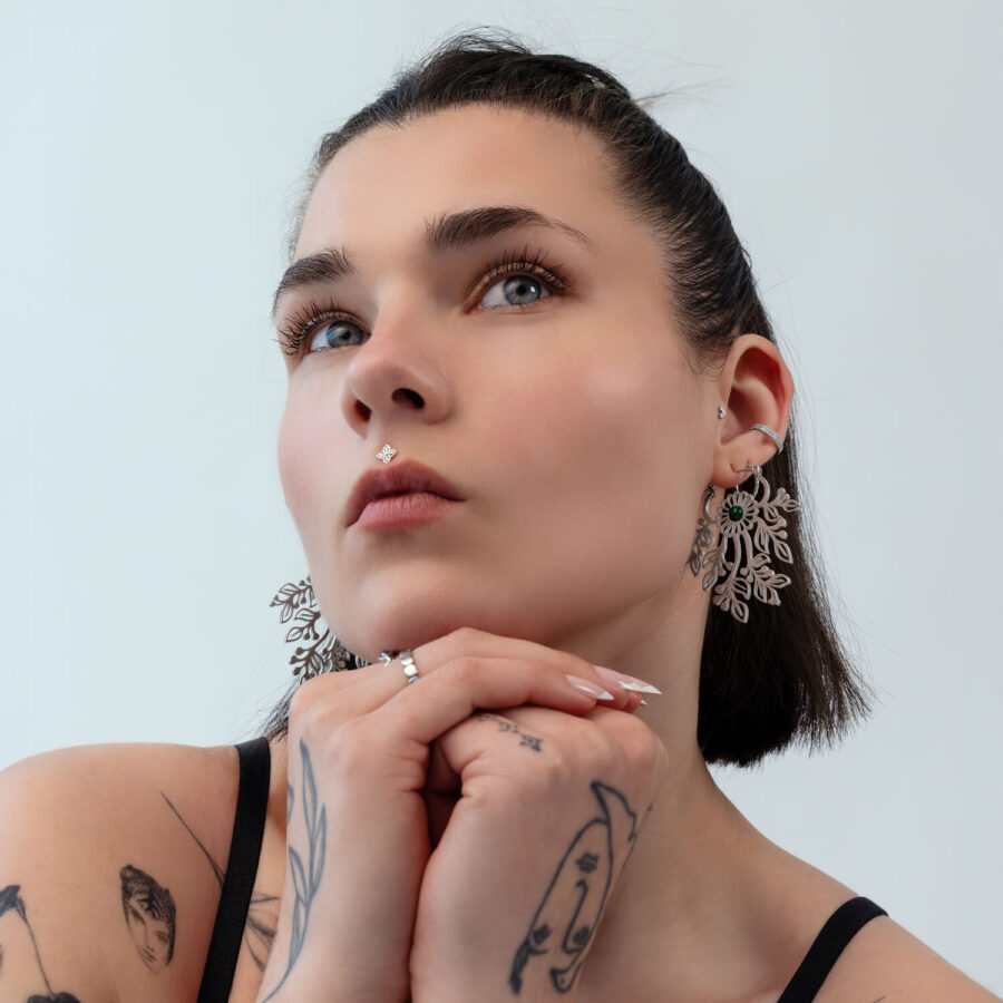 Nainen lyhyillä hiuksilla käyttää suuria, hienostuneita korvakoruja hopeanvärisestä metallista vaalealla taustalla