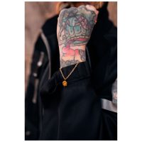 Kultainen rannekoru Smiley-riipuksella tatuoidussa ranteessa
