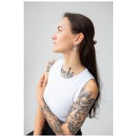 Tyylikkäät Little Flower Hoops -korvakorut Pitkähiuksinen nainen käyttää tyylikkäitä Little Flower Hoops -korvakoruja harmaalla taustalla