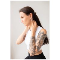 Pitkähiuksinen ja tatuoitu nainen käyttää Little Eye Hoops -korvakoruja