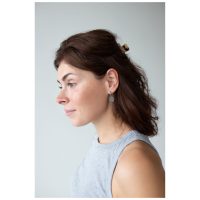 Nainen ruskeilla hiuksilla käyttää Little Luminous Eye Hoops -korvakoruja, sivukuva