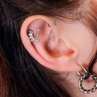 Korvakoru Triple Labret Pushfitillä Lähikuva korvasta, jossa on useita kimaltelevia lävistyksiä, mukaan lukien Triple Labret Pushfit, vaalealla taustalla