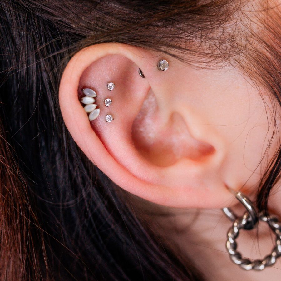 Lähikuva korvasta, jossa on useita kimaltelevia lävistyksiä, mukaan lukien Triple Labret Pushfit, vaalealla taustalla