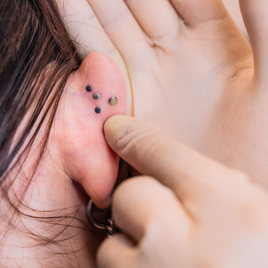 Lähikuva korvasta, jossa on kolme mustaa labret-lävistystä ja sormi koskettaa niitä.