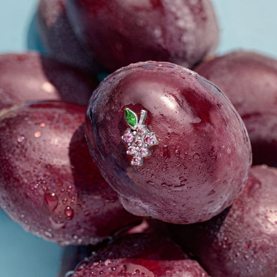 Hopeinen viinirypälekoriste vihreillä lehdillä violetilla luumulla, ympäröitynä muilla luumuilla sinisellä taustalla