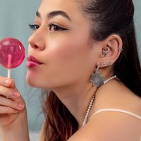 Nainen, jolla on useita hopeisia korvapiercingeitä ja vaaleanpunainen Lollipop, sivulta