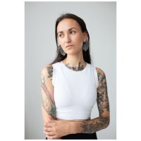 Nainen, jolla on tatuoidut käsivarret, käyttää Monstera Leaf Hoops -korvakoruja, valkoinen toppi