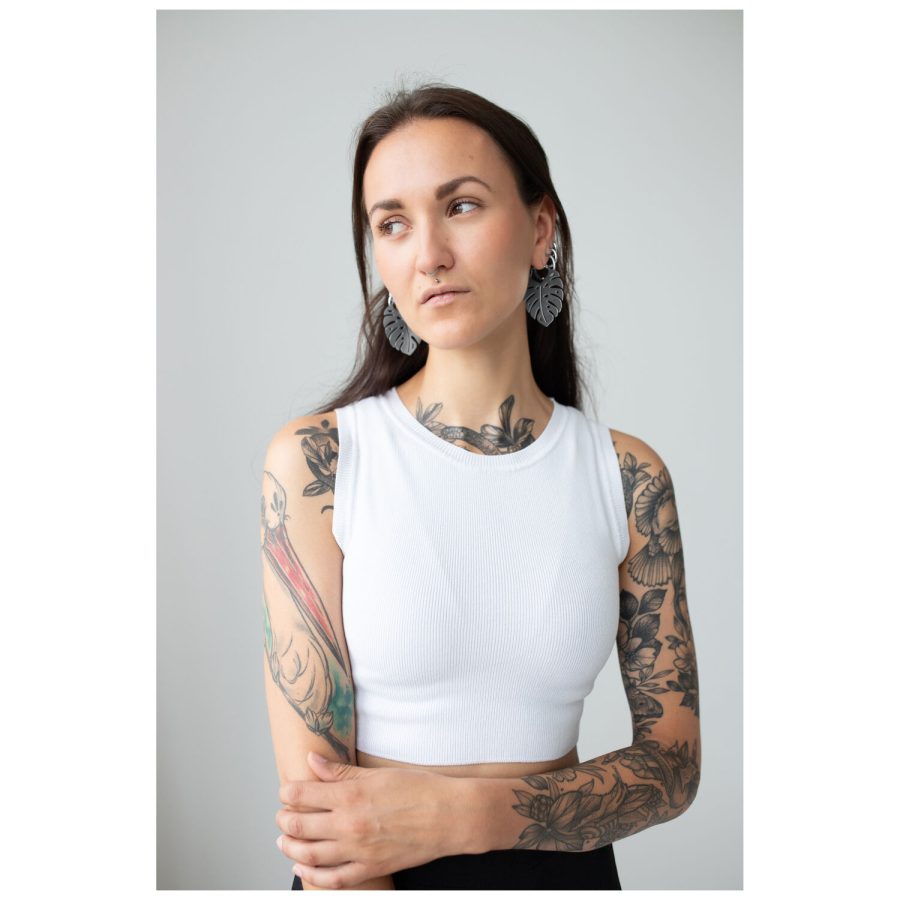 Nainen, jolla on tatuoidut käsivarret, käyttää Monstera Leaf Hoops -korvakoruja, valkoinen toppi
